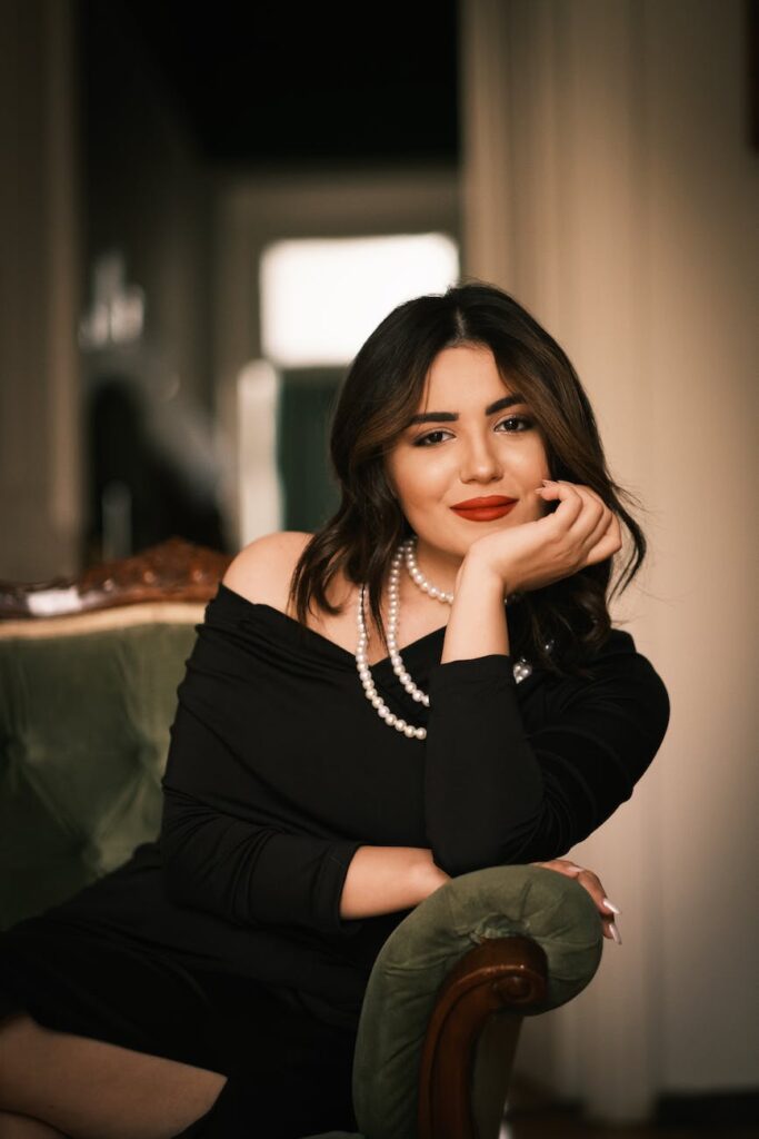 photo of a woman in a black dress and pearls sitting in an armchair